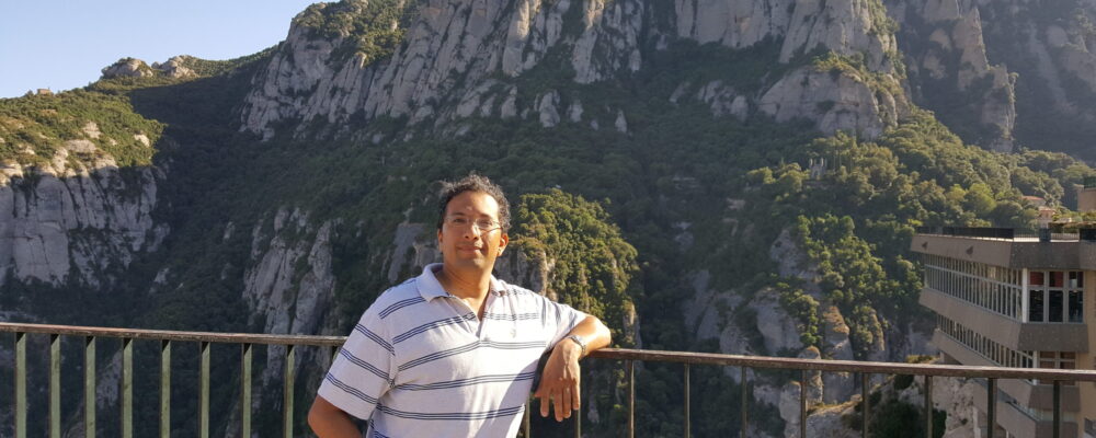 S. Sandeep Pradhan leaning against a railing in front of a mountainous background